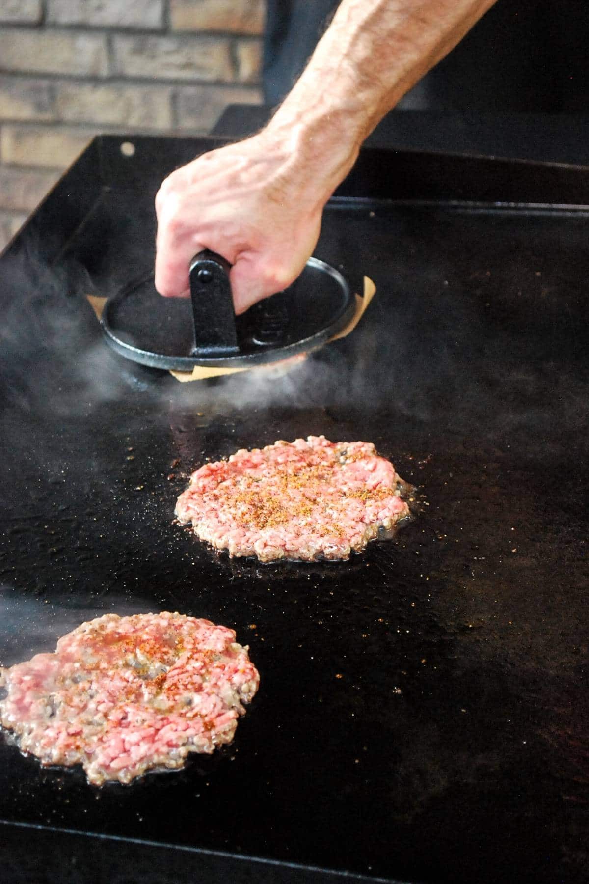 smashing a burger patty on a flat top griddle