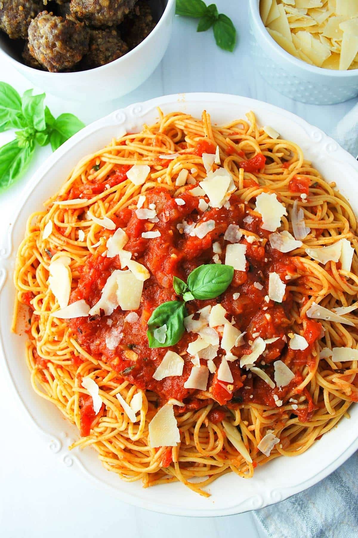 large serving bowl of spaghetti arrabiata topped with fresh basil and parmesan cheese