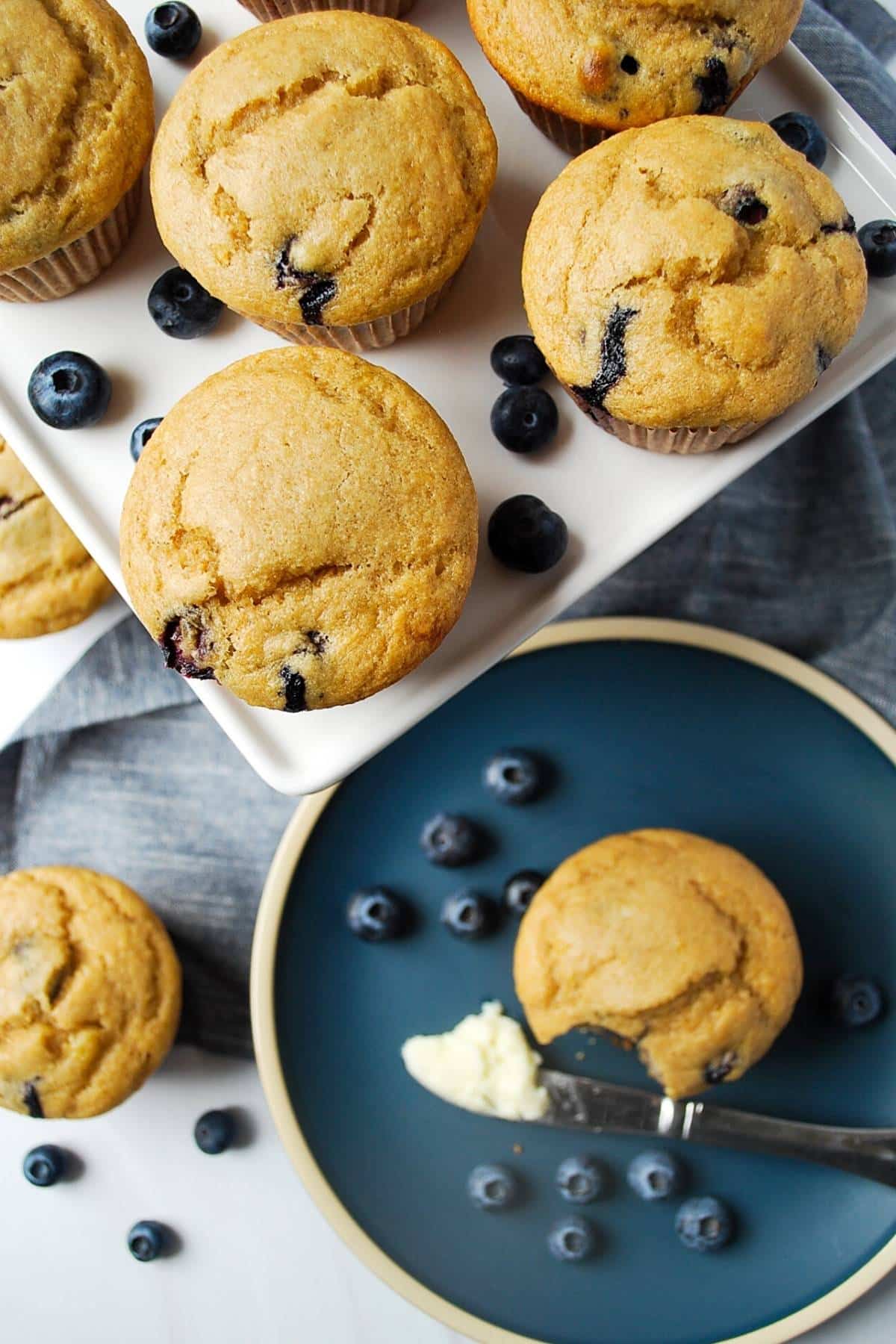 overhead photo of blueberry muffins on a plate and a platter with a pat of butter on a knife