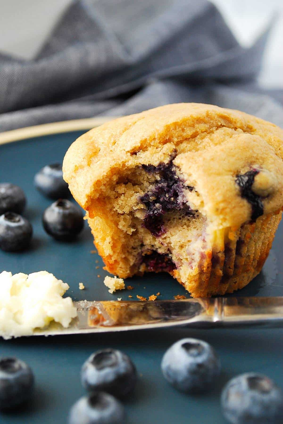 photo of a blueberry muffin with a bite out of it on a plate with blueberries 