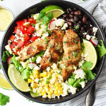 close up of a Mexican grilled chicken salad in a bowl with queso fresco cheese, beans, tomatoes, corn, greens, and lime