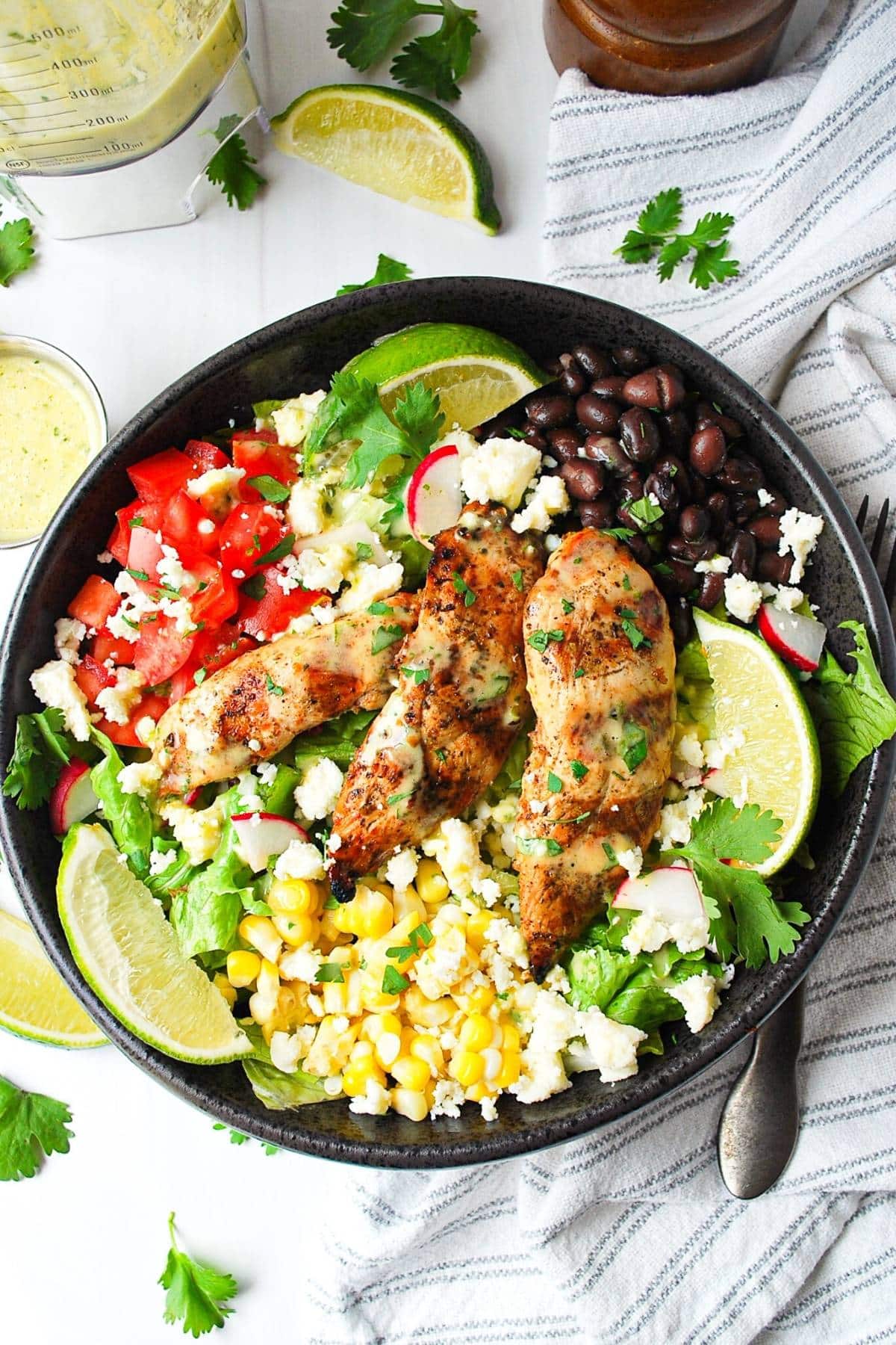 a bowl of Mexican chicken salad with corn, grilled chicken, tomatoes, black beans and fresh lime