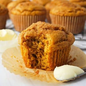 close up of a pumpkin muffin with a bite out of it with a knife with butter on it