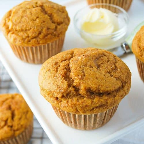 pumpkin muffins on a white platter with a dish of butter and a knife