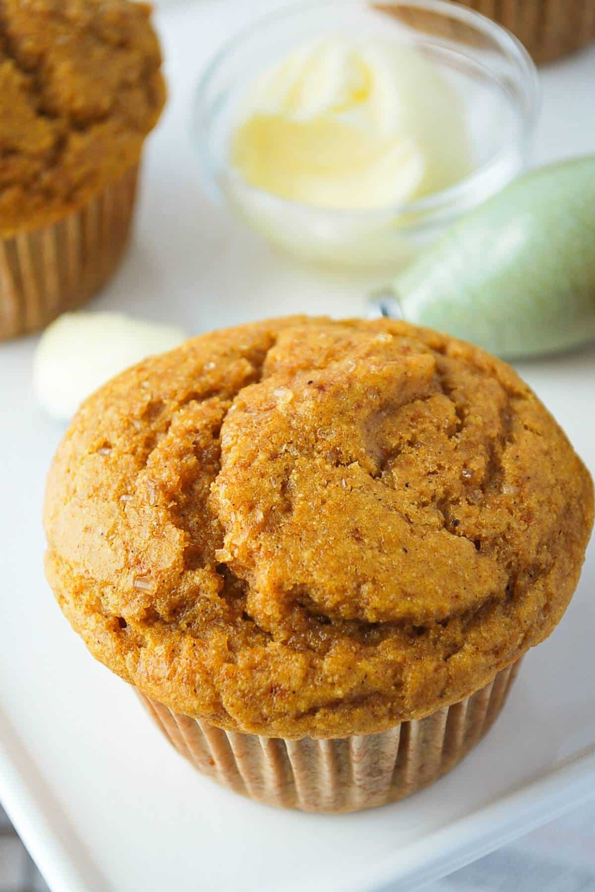 a pumpkin muffin on a white platter with a knife and butter behind it