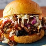 close up of a pulled pork sandwich with slaw and dripping with bbq sauce