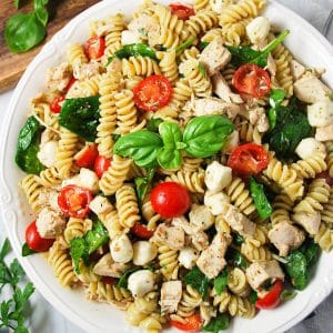 overhead photo of a bowl of chicken pesto pasta salad with a sprig of fresh basil