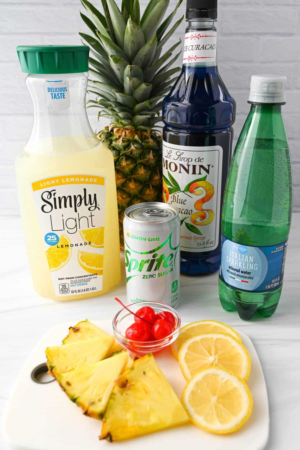 ingredients for a blue lagoon mocktail on a counter with a whole pineapple in the background