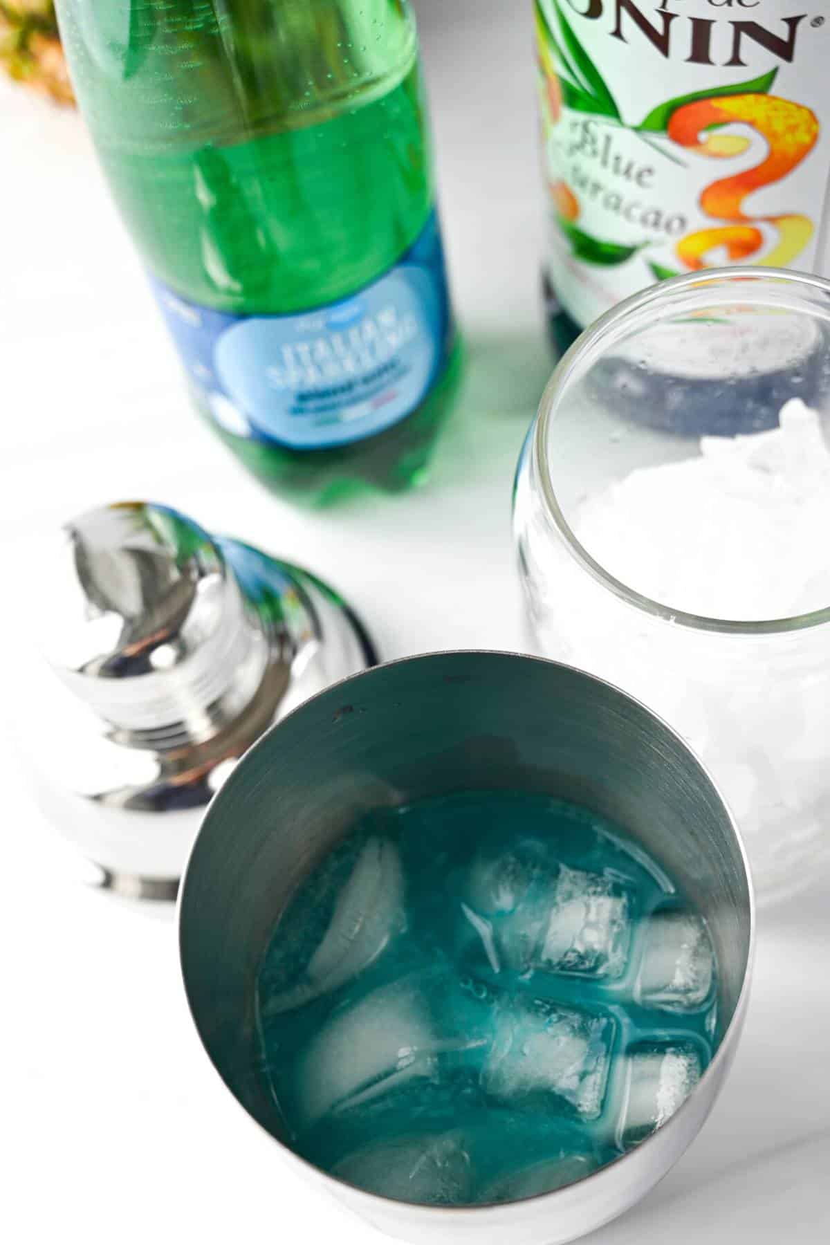 blue curacao syrup mixed with lemonade and ice in a cocktail shaker with ice