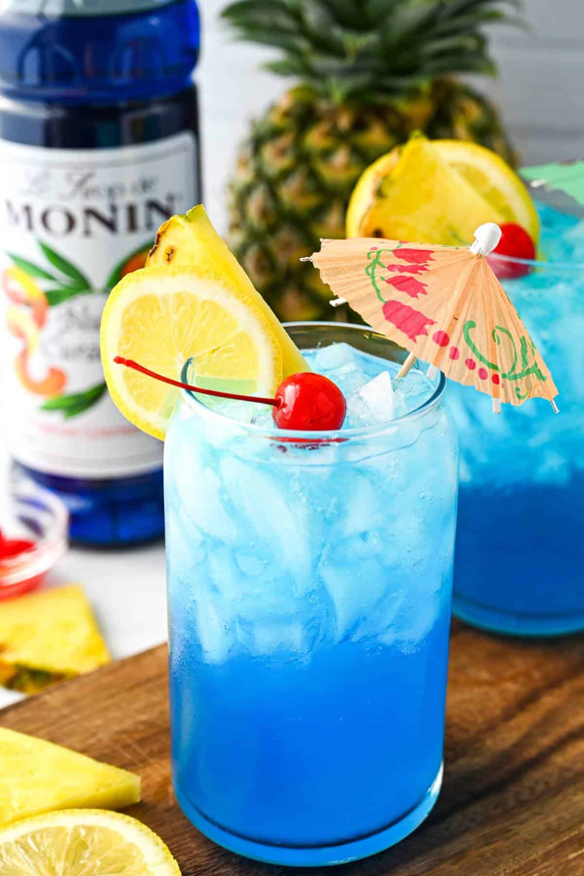a bottle of monin blue curacao syrup behind a could of blue non-alcoholic drinks with fancy tropical garnishes
