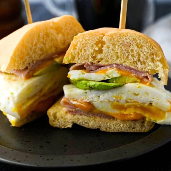 a gluten free breakfast sandwich with egg, avocado, cheese, and ham sliced in half
