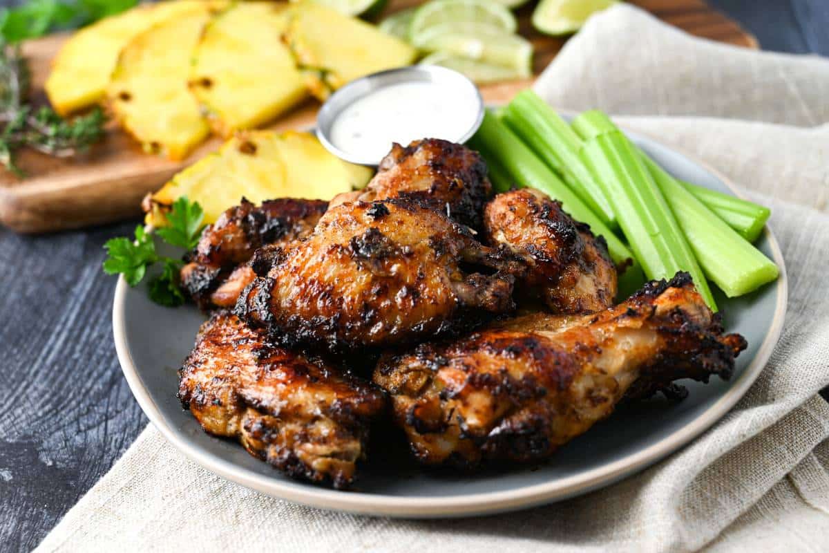 jerk chicken wings served on a plate with ranch, celery, and a pineapple slice with a sprig of parsley