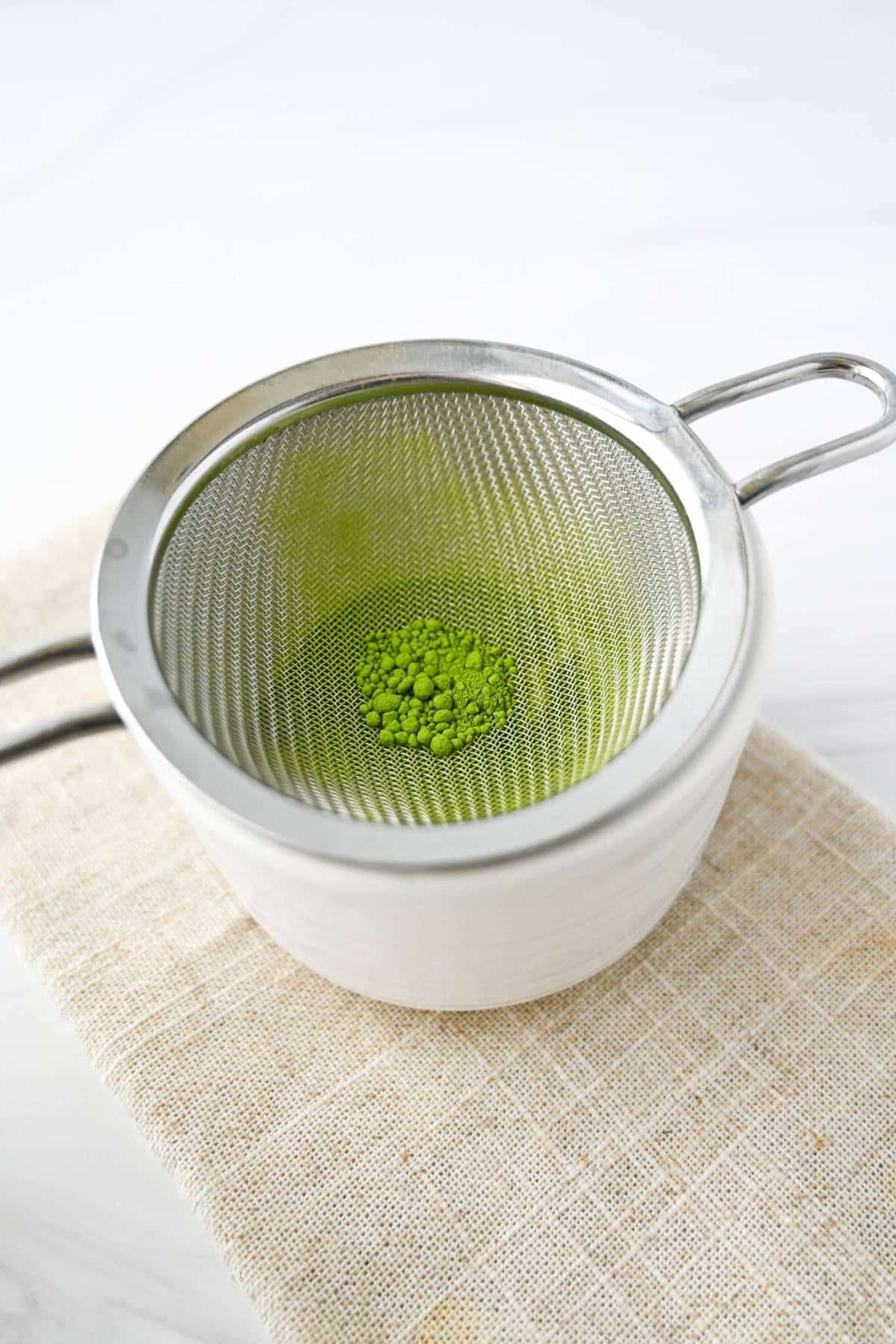 sifting matcha in a mug with a small sieve