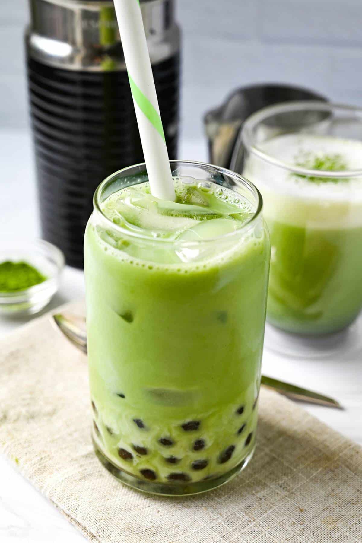 a glass of green tea milk tea with boba and a straw 