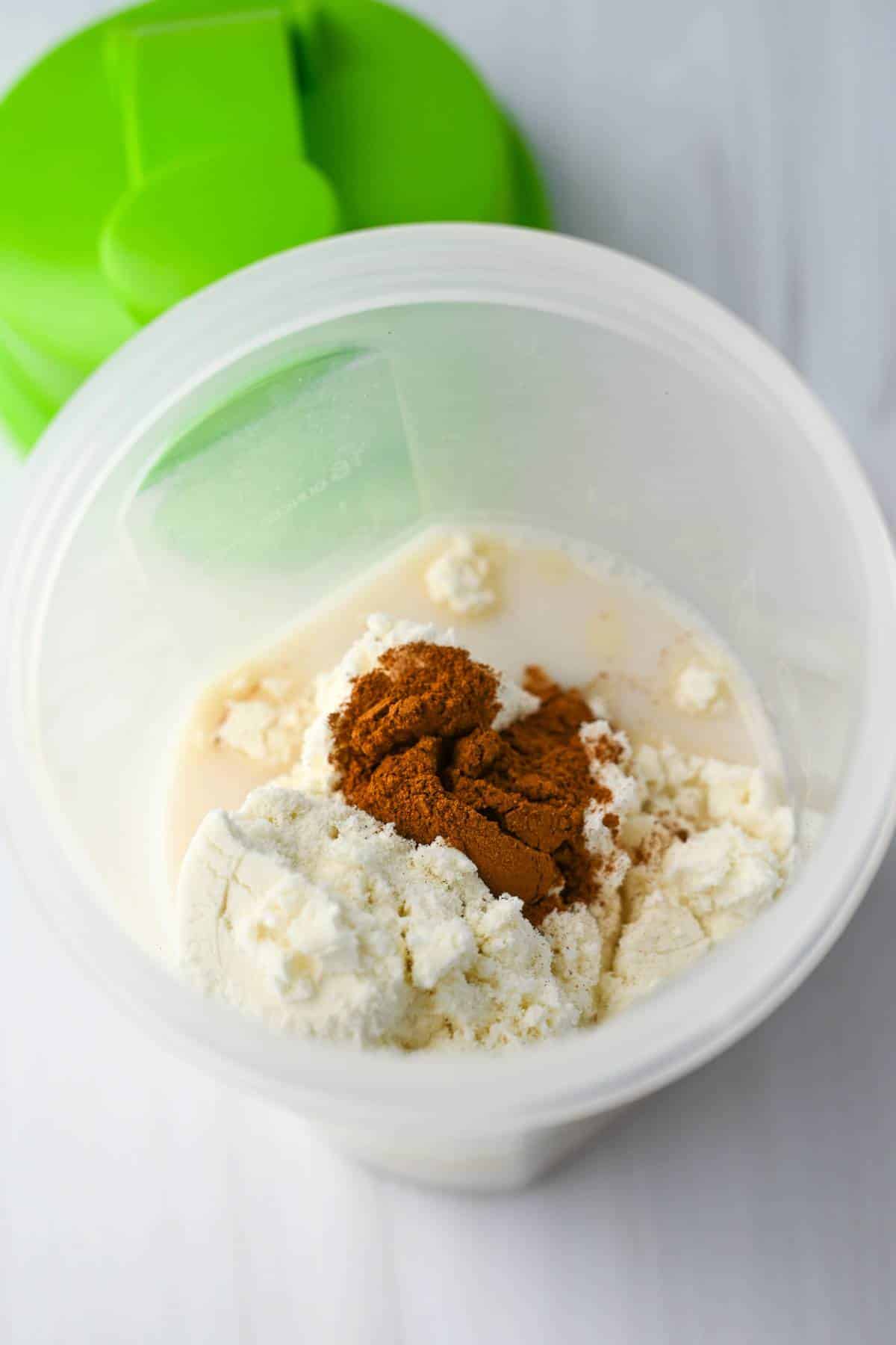 shaker bottle with whey, cinnamon, and almond milk ready to mix