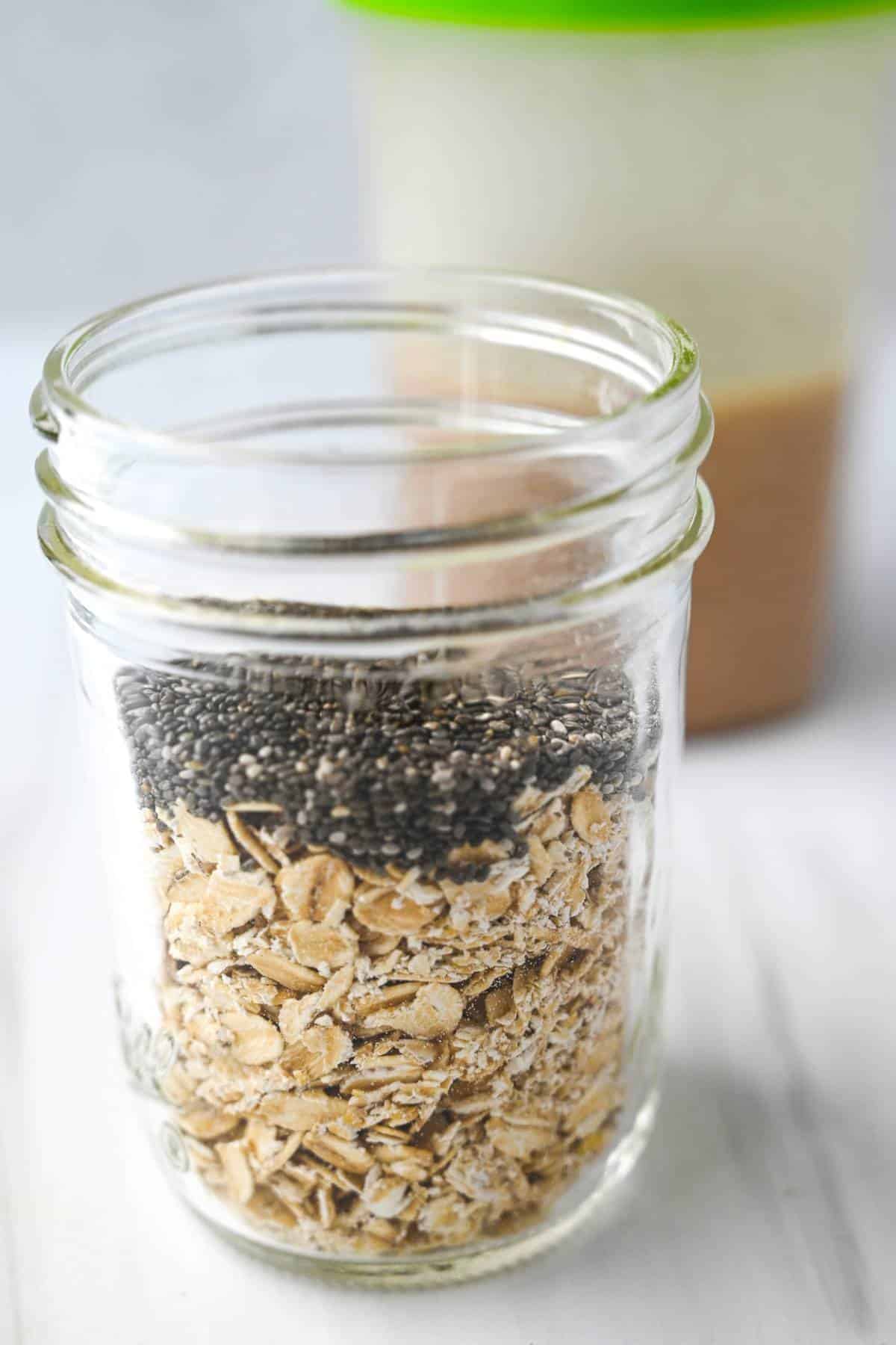 oats and chia seeds in a jar with shaker bottle of milk mixture behind it