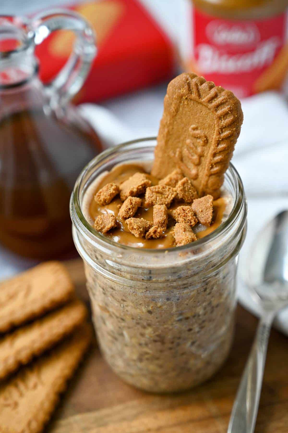 a mason jar of protein overnight oats with biscoff cookie butter and crumbled biscoff on top with a spoon on a wooden surface