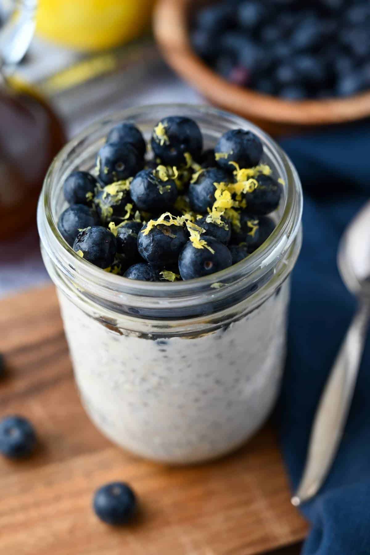 side view of a jar of cheesecake oats topped with blueberries and lemon zest