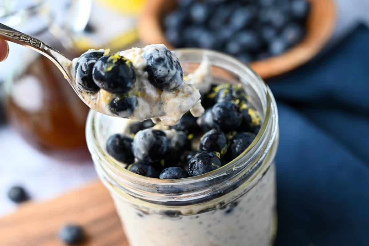 a spoonful of cheesecake oats with blueberries over a mason jar