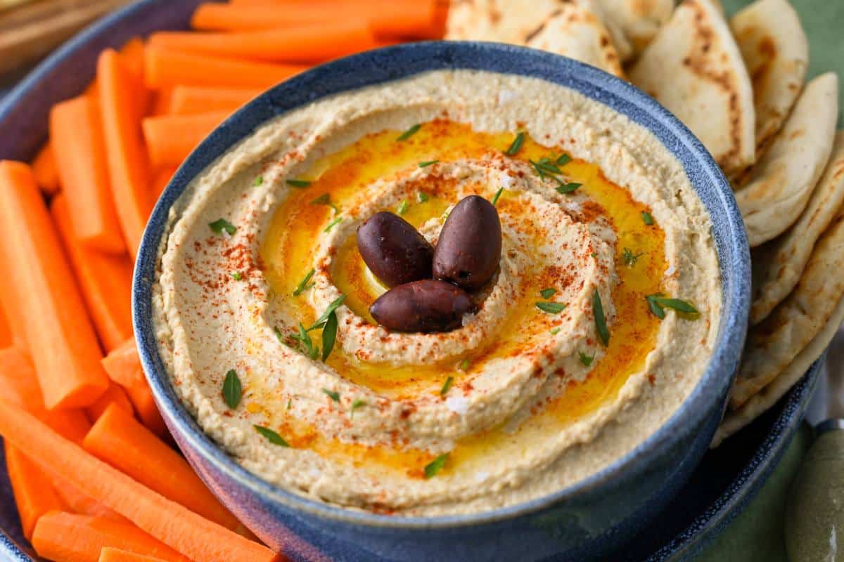 a bowl of hummus garnished with olive oil, olives and parsley