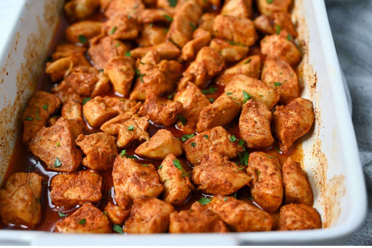 side view of a white serving dish with chicken bites in a spicy sauce with a napkin next to it