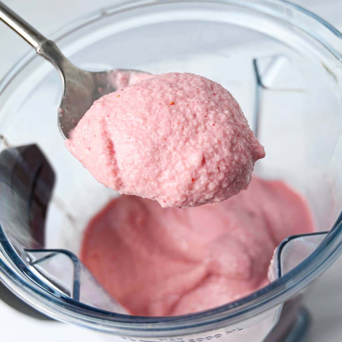a spoonful of soft serve strawberry ice cream over a blender container