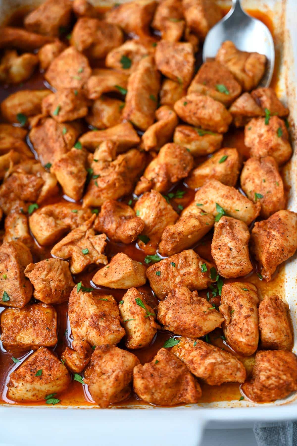 a pan of bite size baked chicken bites with a spicy seasoning with a spoon
