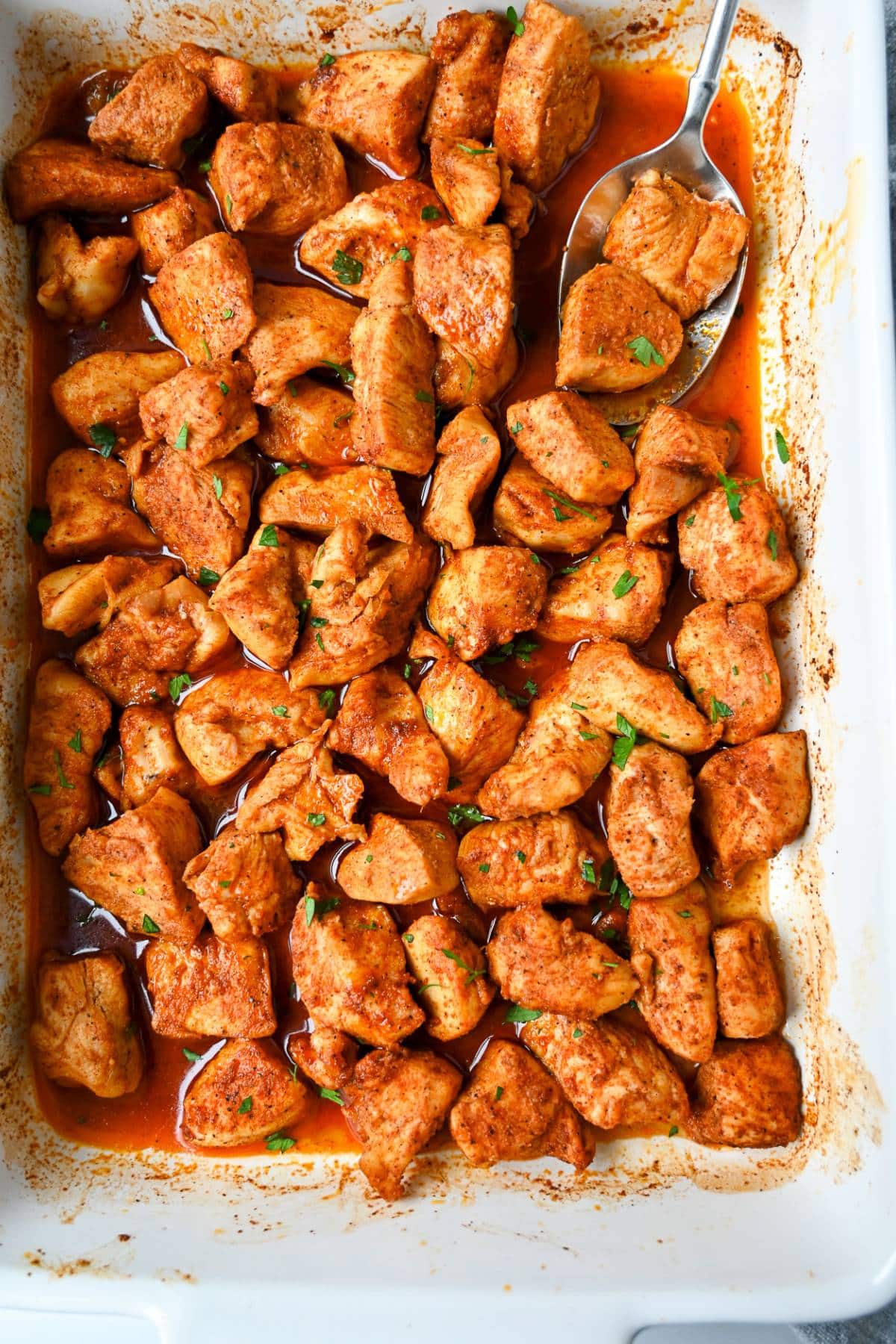 a zoomed out photo of a pan of bite size chicken pieces baked in a spicy sauce with pan juices