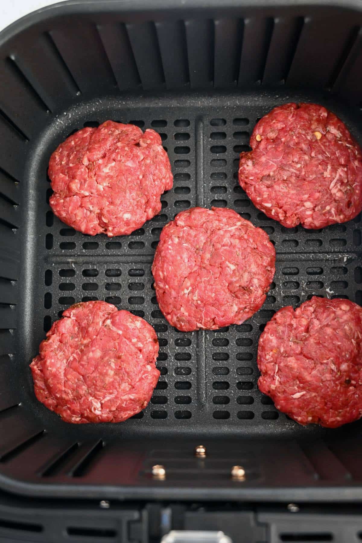 beef sausage patties in an air fryer basket ready to cook