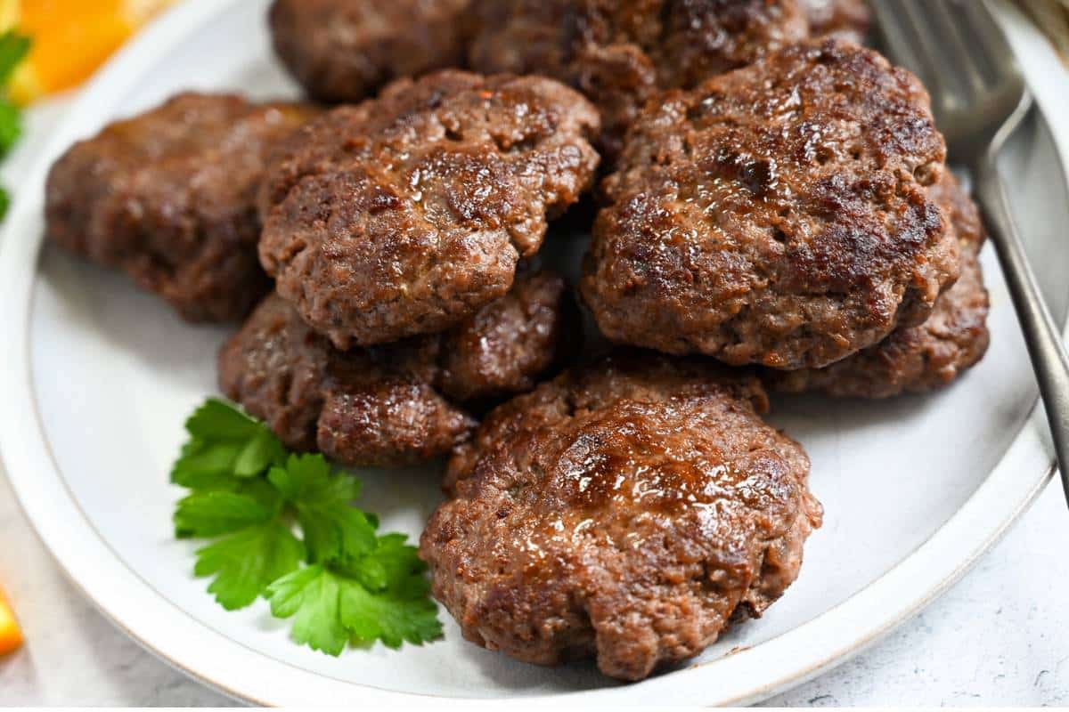 side view of stacked beef breakfast sausage on a plate with a fork