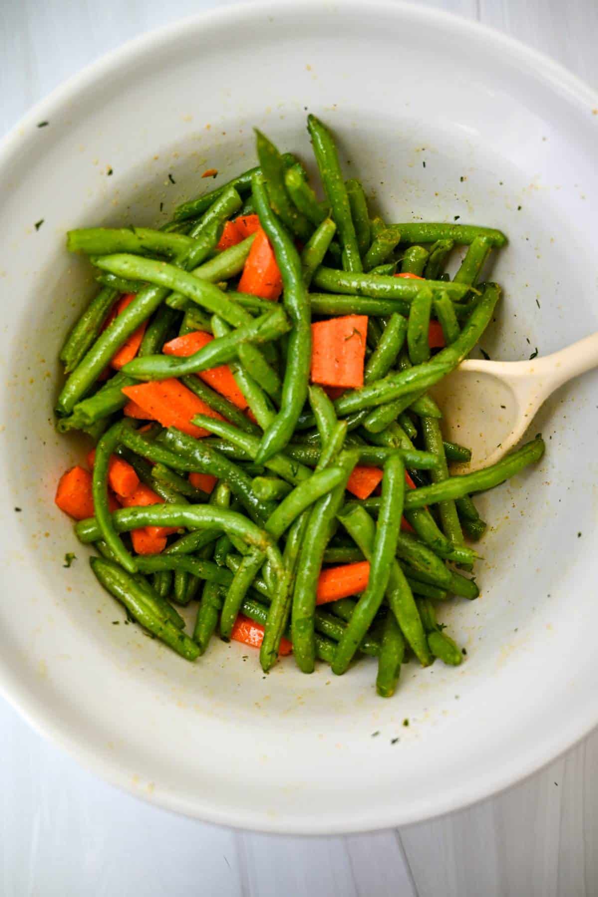 fresh carrots and green beans tossed with olive oil and seasonings in a white bowl