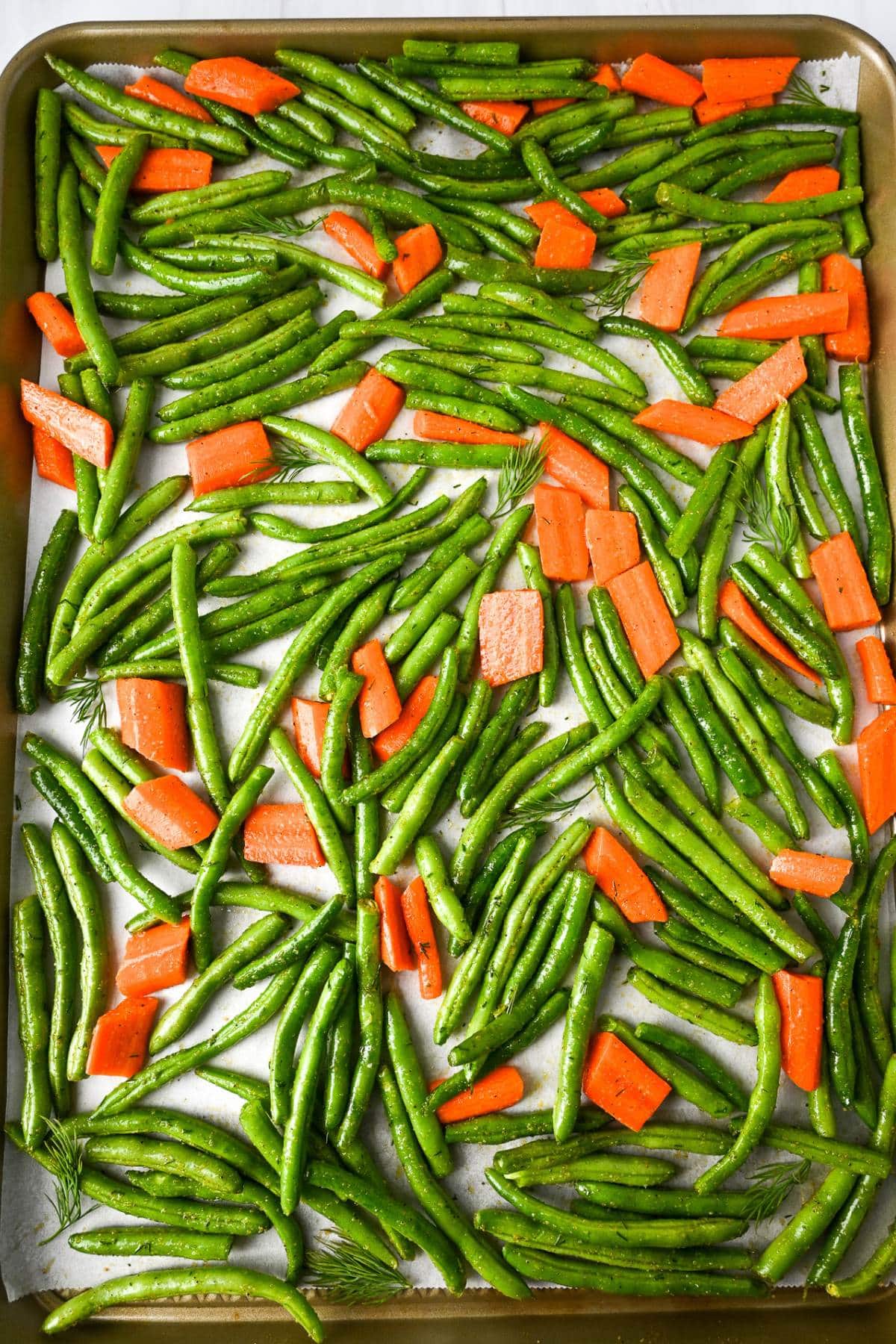 green beans and carrots spread onto a parchment lined sheet pan ready to roast