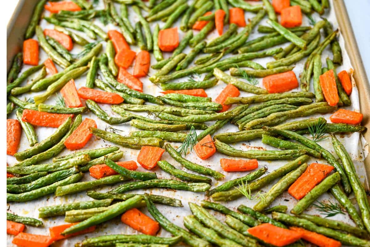side view of roasted carrots and green beans on a baking sheet with fresh herbs