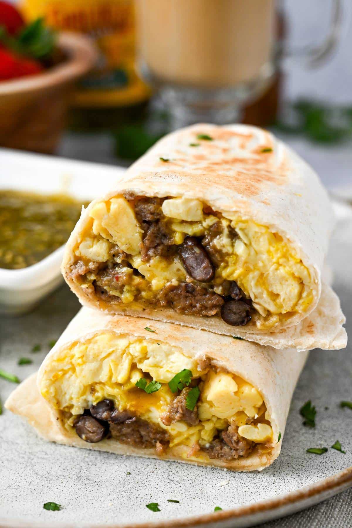 a stacked sliced breakfast burrito next to a dish of salsa verde