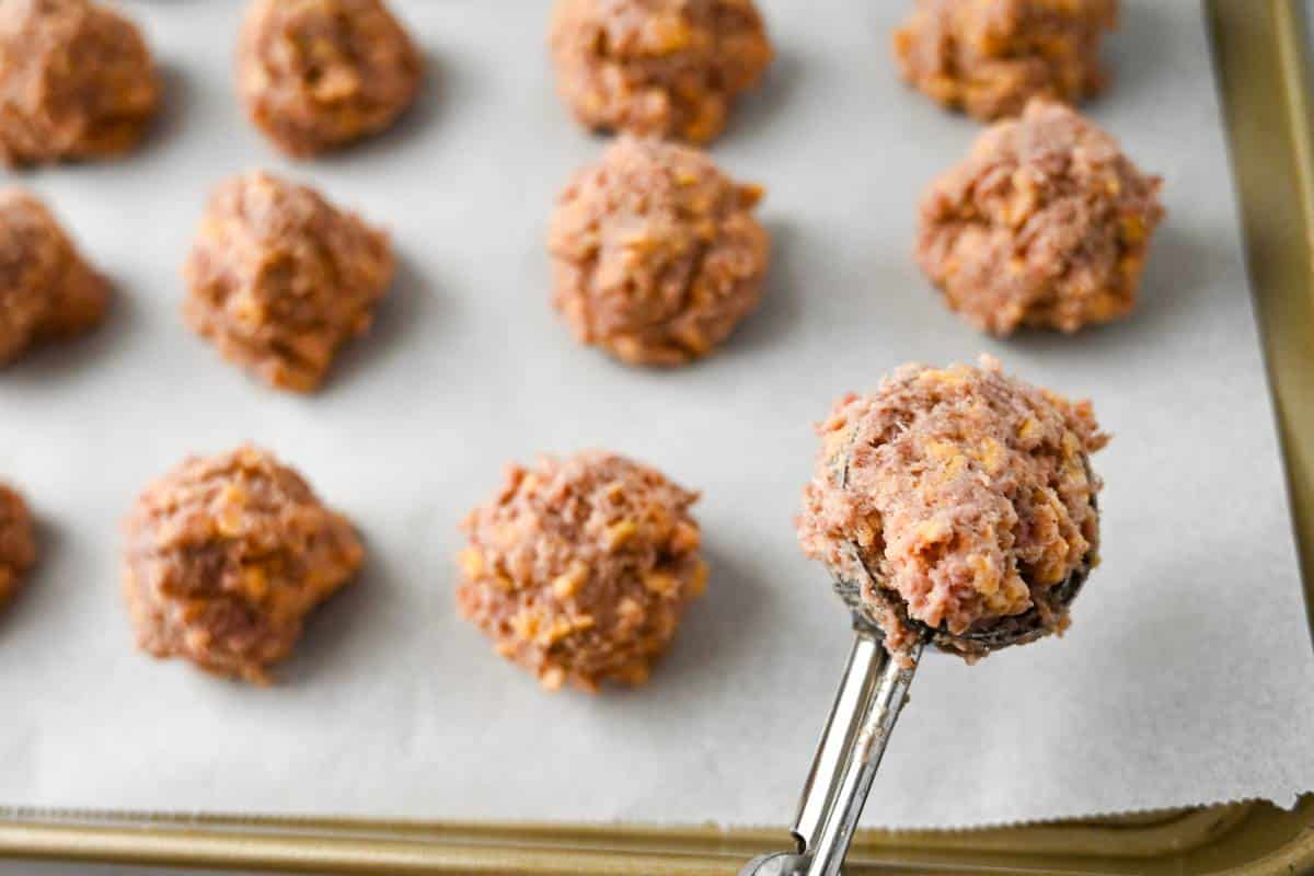 sausage balls being scooped onto a parchment lined baking sheet 