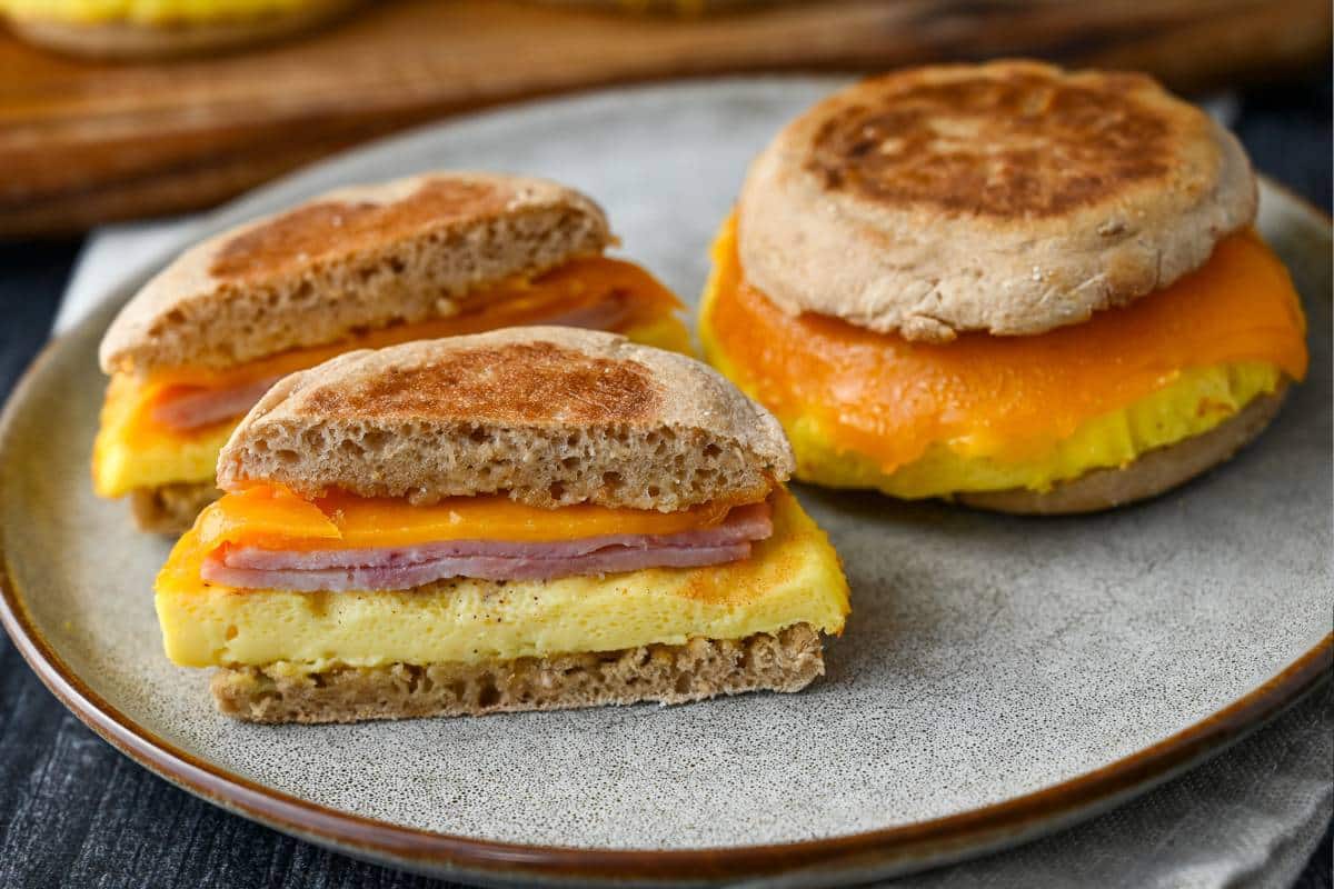 a sliced copycat egg mcmuffin sandwich on a plate next to a whole unsliced sandwich
