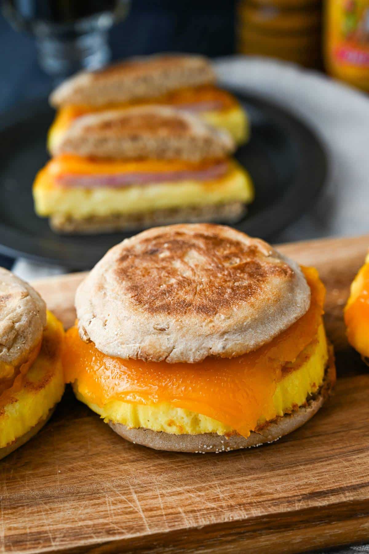 zoomed in on a healthy egg muffin breakfast sandwich with melting cheese and a sliced sandwich behind it