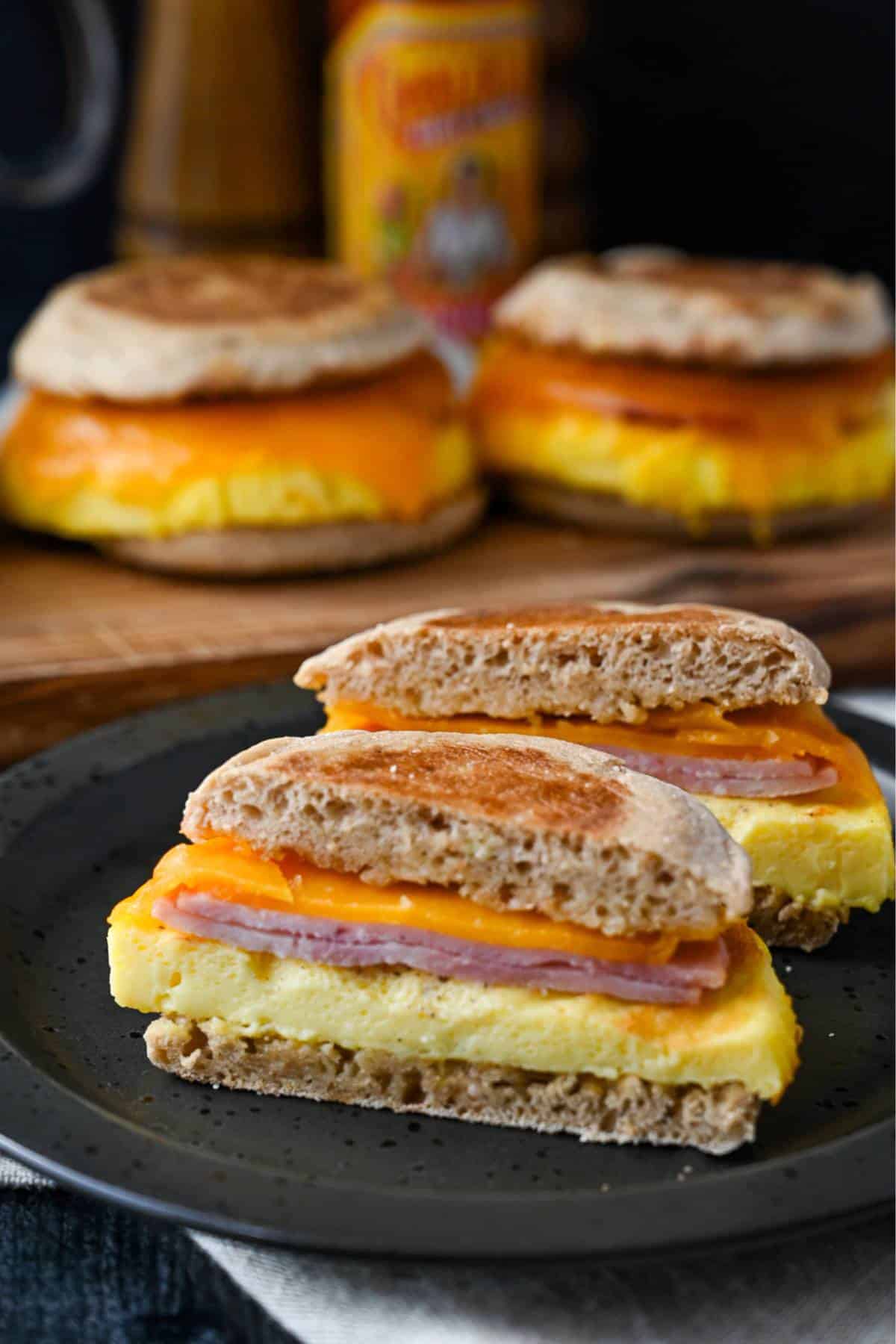 a homemade egg mcmuffin sliced in half with 3 egg mcmuffins on a serving board behind it with a bottle of hot sauce