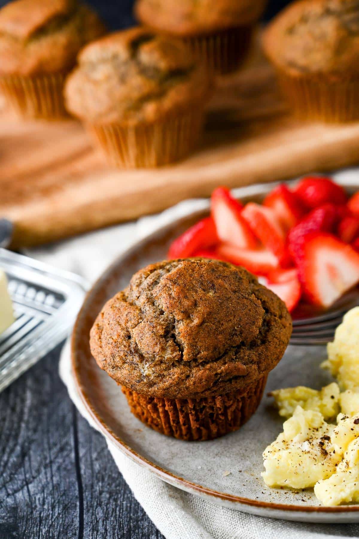 a banana muffin on a plate with scrambled eggs and strawberries with muffins in the background