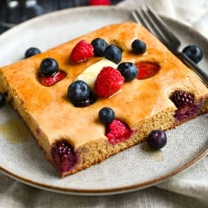 a large slice of protein pancake made in a sheet pan and topped with butter, berries and syrup