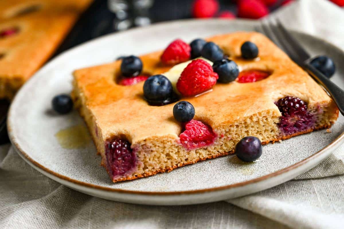 close up of a slice of protein pancake baked in a sheet pan with berries