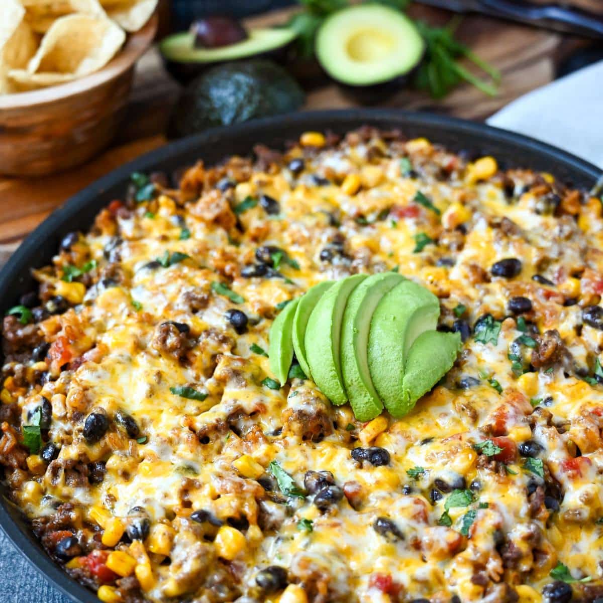 cheesy beef and rice skillet with an avocado and chips in the background