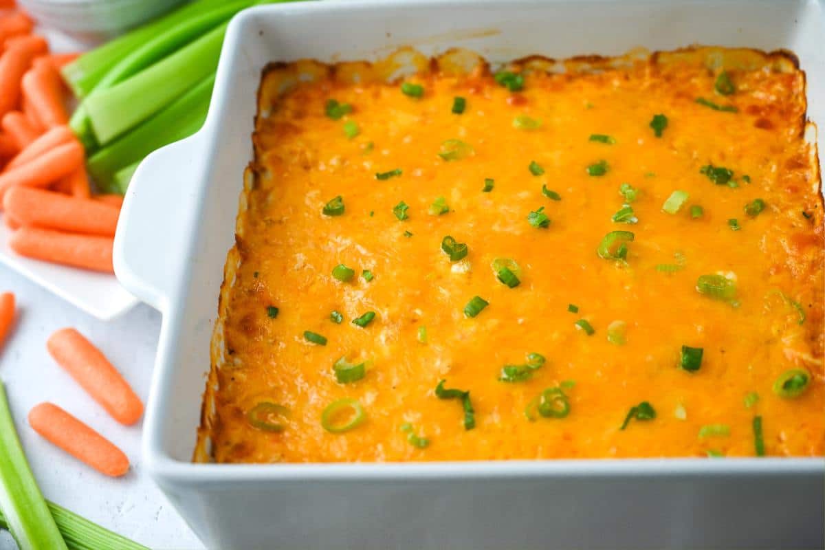 side view of a pan of baked buffalo chicken dip with baby carrots and celery sticks