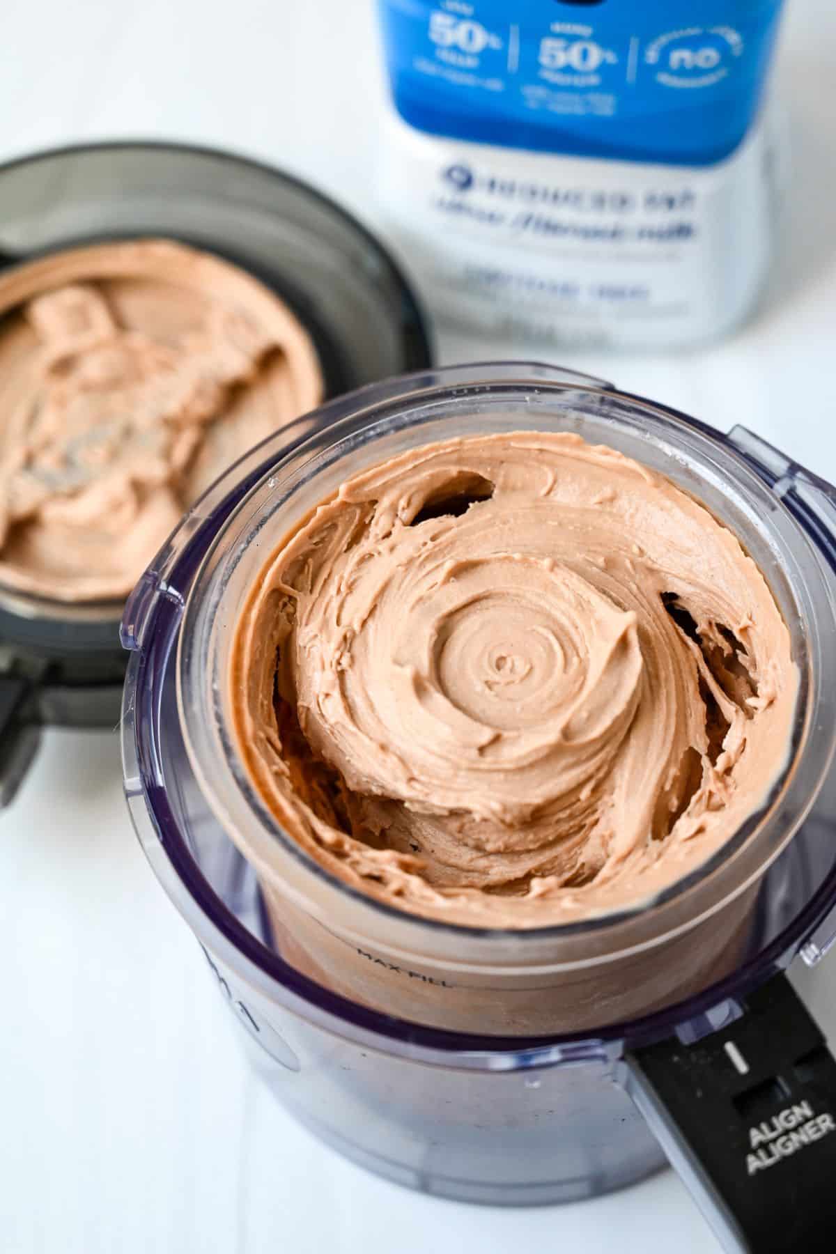 chocolate protein ice cream blended in a creami container with a jug of milk behind it