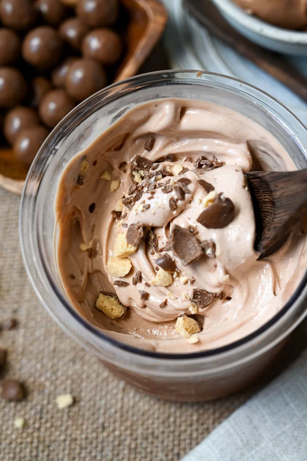 overhead photo of chocolate protein ice cream with crushed malt balls in a ninja creami container