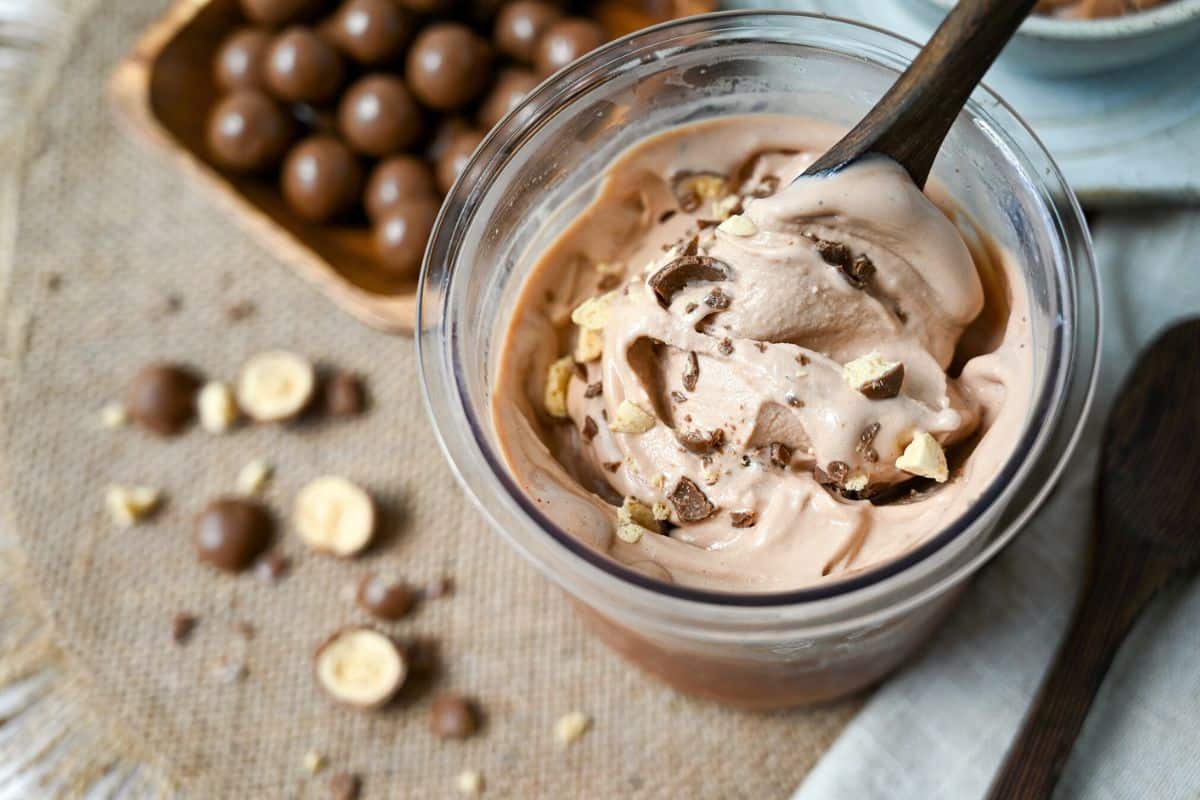 a container of chocolate protein ice cream with malt balls blended in made in a ninja creami