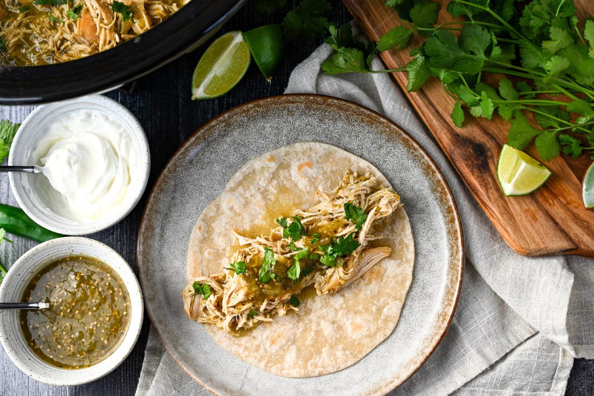 a shredded chicken taco on a plate with cilantro and garnishes around it