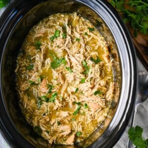 a zoomed in photo of green chili chicken in a crockpot with fresh cilantro on top