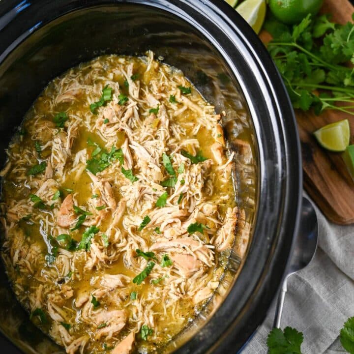 shredded chicken in salsa verde in a slow cooker topped with fresh chopped cilantro