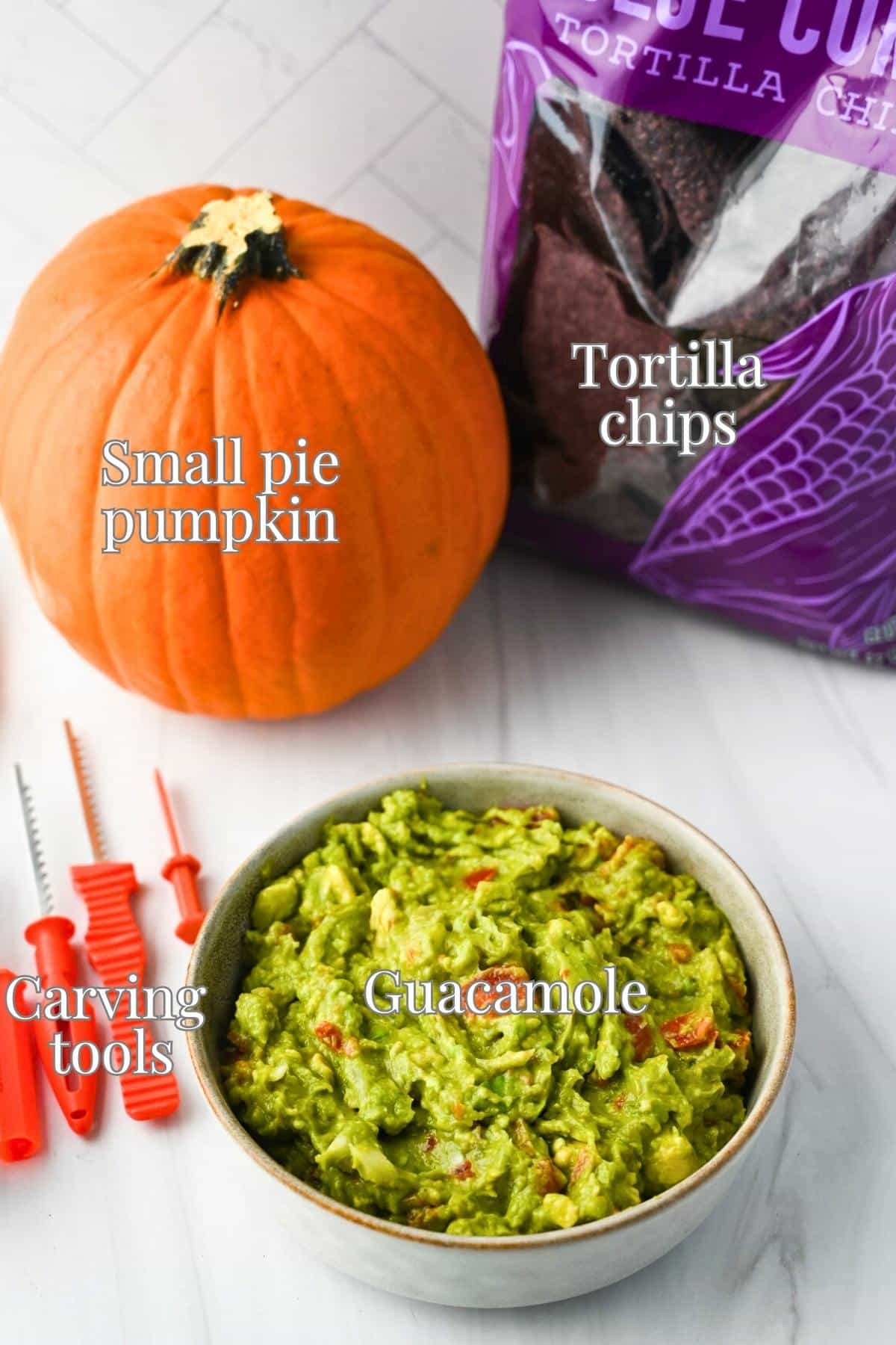 a pumpkin, bowl of guacamole, bag of chips, and carving tools on a counter